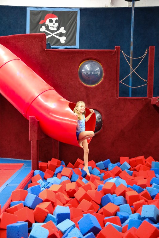 Young girl sitting above foam pit on bottom of red slide